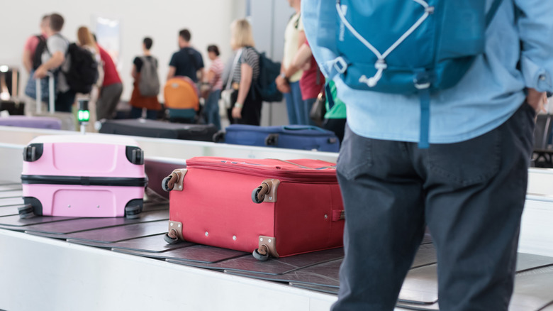 Luggage on conveyor belt at baggage claim with passengers waiting