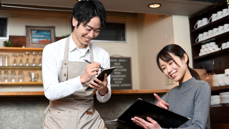 A woman orders from a waiter in a cafe