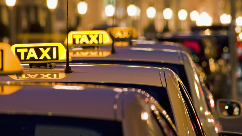 Taxis with lit signs lined up with street lamps in the background