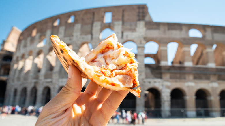 Hand holding pizza by the coloseum