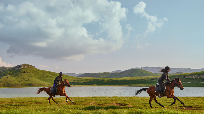 two horse riders by lake