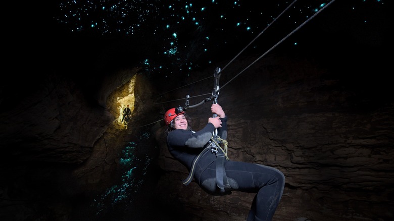 Caver slides down underground zip-line with glow worms overhead