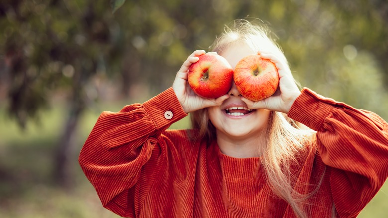 Child holding apples over her eyes