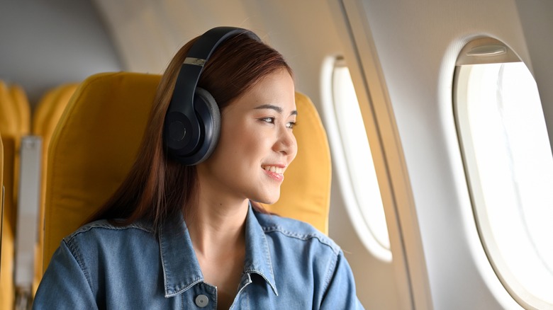 woman wearing headphones looking out plane window