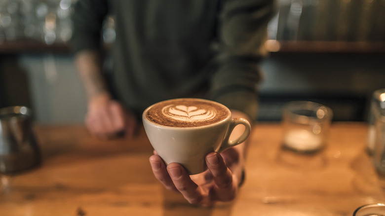 barista holding out cup coffee