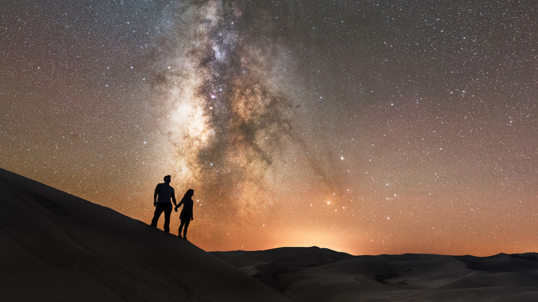 Hikers looking at night sky atop a sand dune