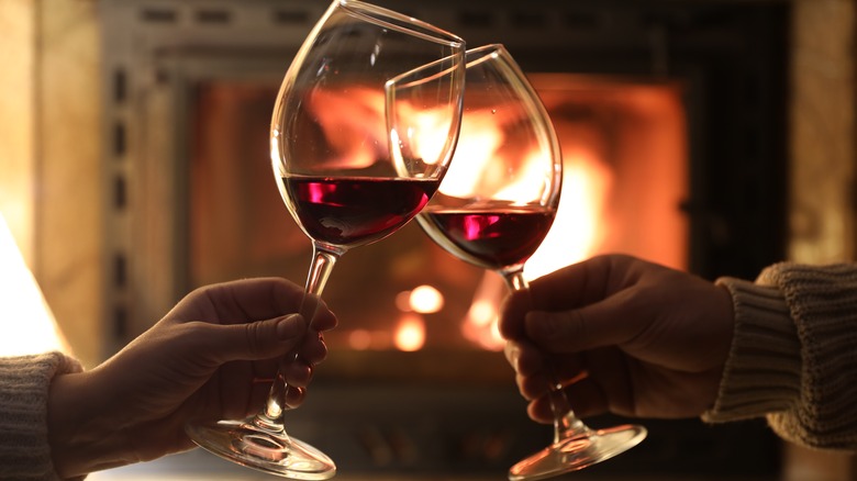 Hands clinking wine glasses near a fire