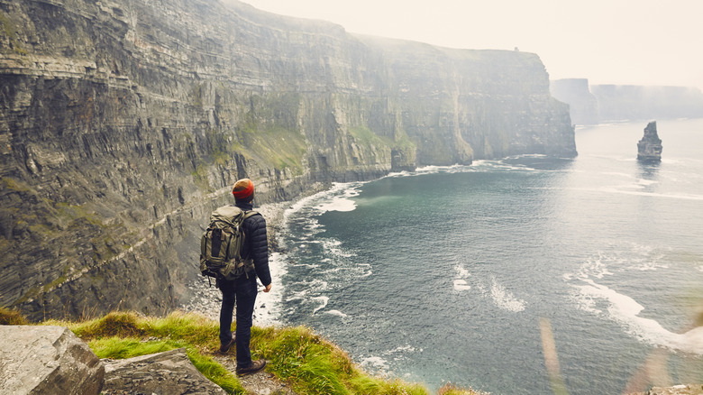 Backpacker gazes out at cliffs on Irish coast