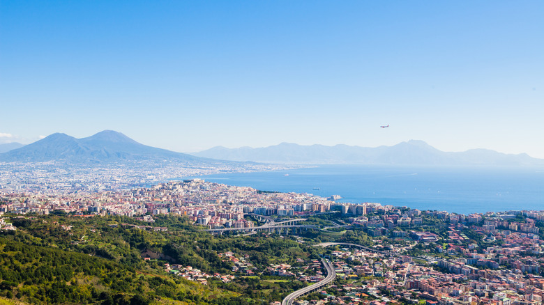 Plane flying over ocean, mountains, and city of Naples