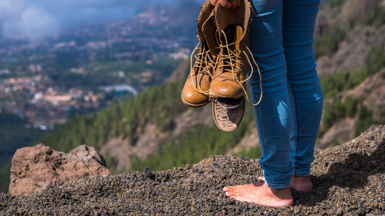 Barefoot hiker holding broken boots