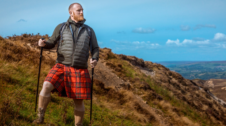 A hiker wears a kilt on top of a grassy hill.