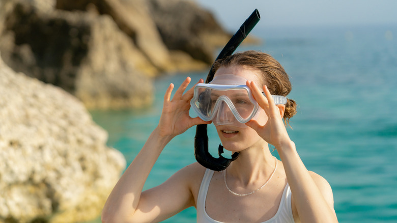 Woman wearing snorkel mask and breathing tube with faded ocean background