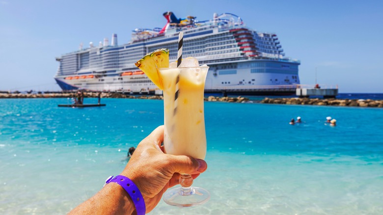 Hand holding cocktail near cruise ship