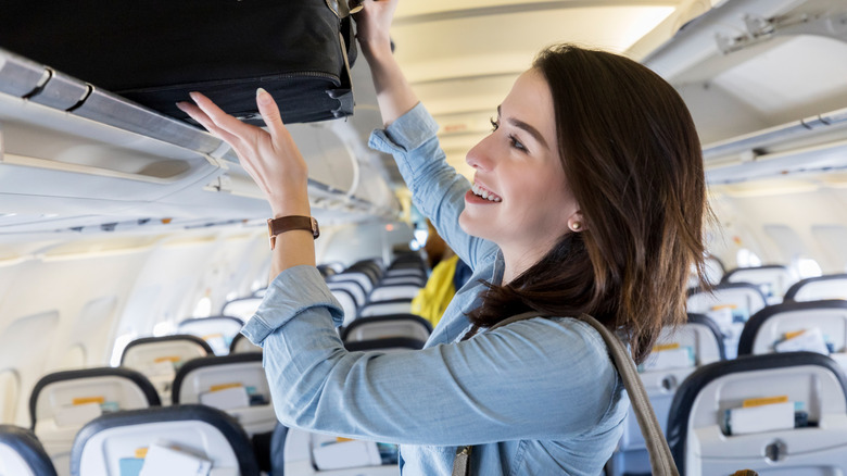 Woman taking suitcase out of overhead compartment