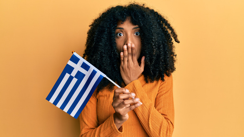 a woman with a hand over mouth and holding a Greek flag