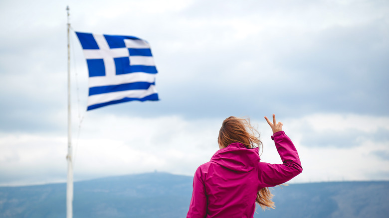 a person holding up a peace gesture in front of Greek flag