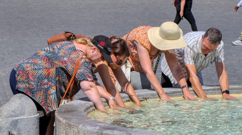 Tourists putting hands in fountain