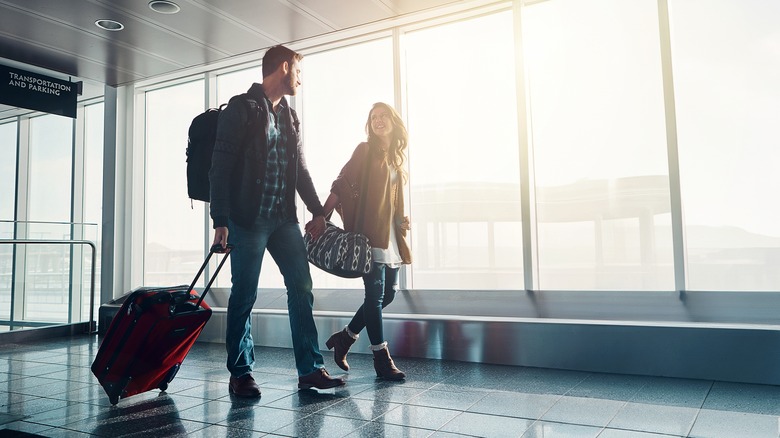 couple looking at each other and walking through airport with bags