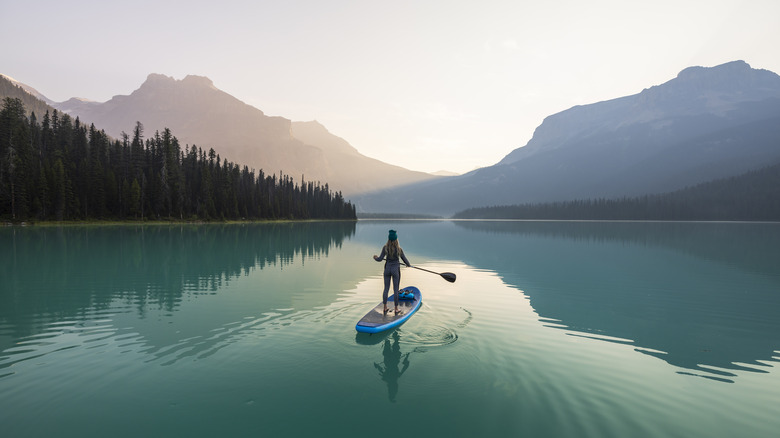 woman on stand-up paddleboard on turquoise lake with mountain backdrop