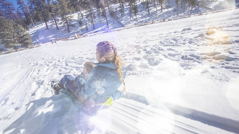 Woman and child sledding together down a snowy hill