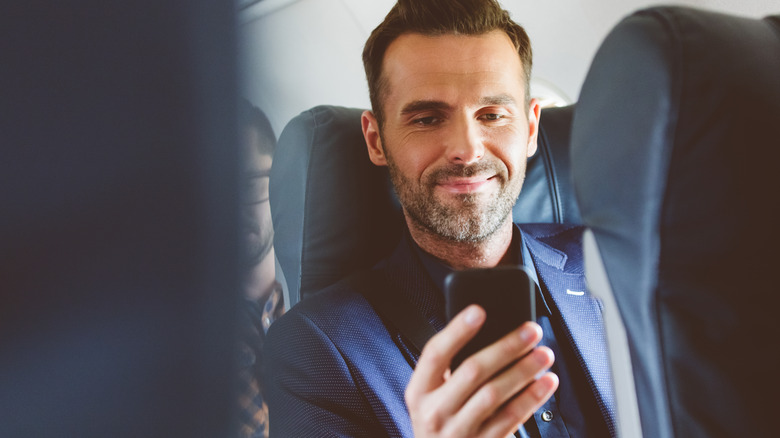 man smiling at phone on airplane
