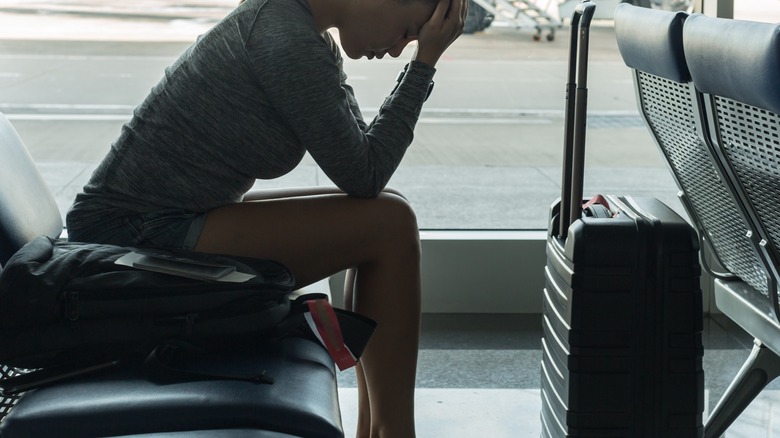 A sad woman sits in an empty airport with her head in her hands.