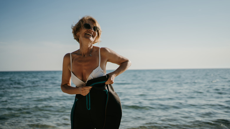 Smiling woman putting on wetsuit