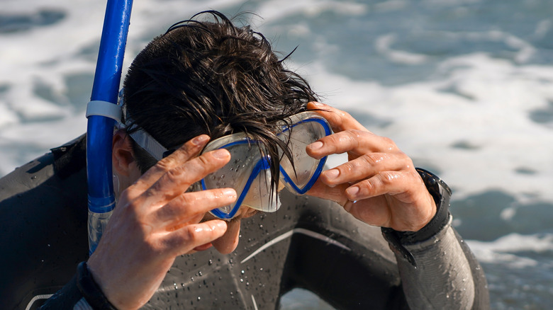 Snorkeler in a wetsuit removing goggles