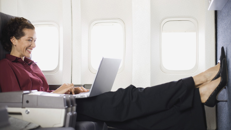 Woman working on a laptop in a plane seat with extra leg room