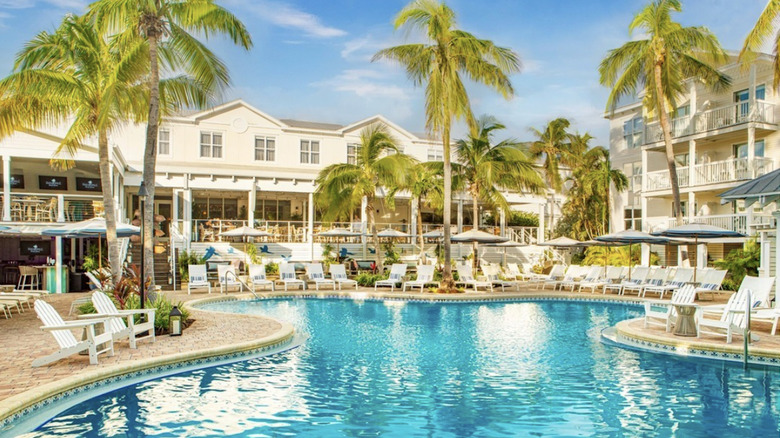 A turquoise pool surrounded by beach chairs and buildings.