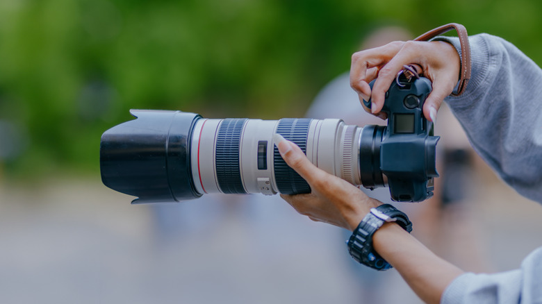 Hands hold a large telephoto lens outdoors