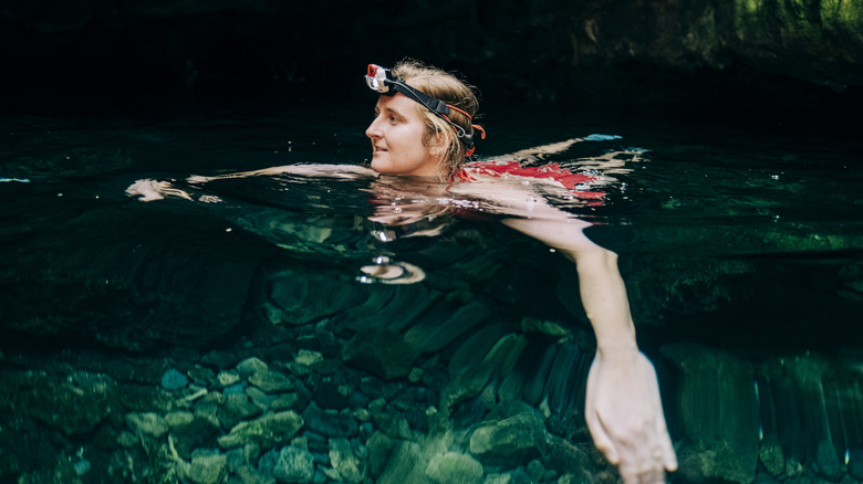 Woman swimming in cave with headlamp on