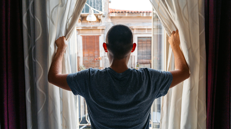 man opening window curtains