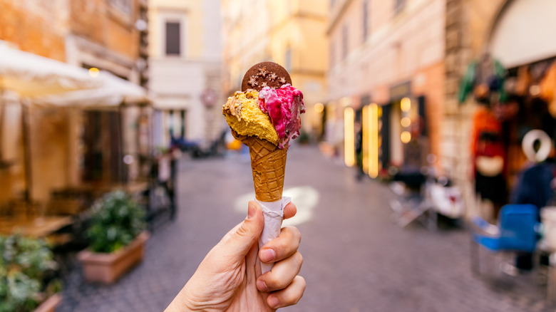 Gelato cone held in a hand, with an Italian street out of focus in the background.