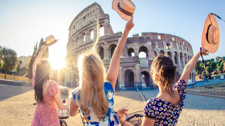 Women waving hats near Roman ruin