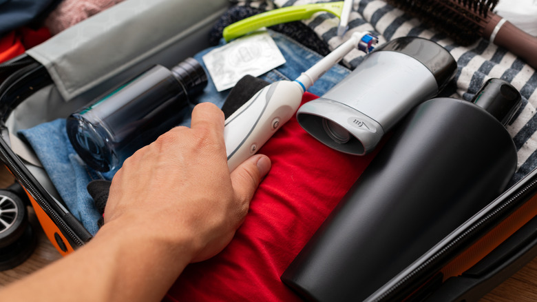 hand putting toothbrush in suitcase