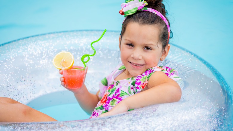 Child holding colorful drink in pool