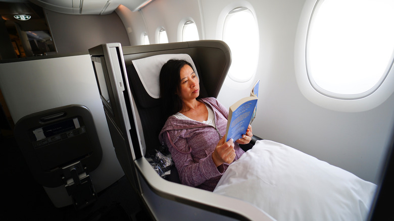 A woman in first class lounges while reading a book.