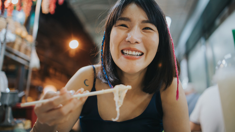 Smiling traveler eating Thai food with chopsticks
