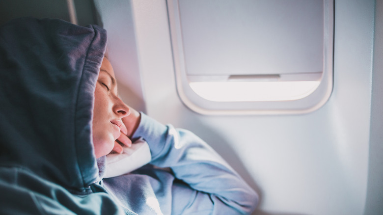 Woman with hood sleeping on plane next to window seat