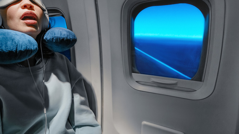 Woman sleeping on plane with neck pillow, eye mask, and headphones