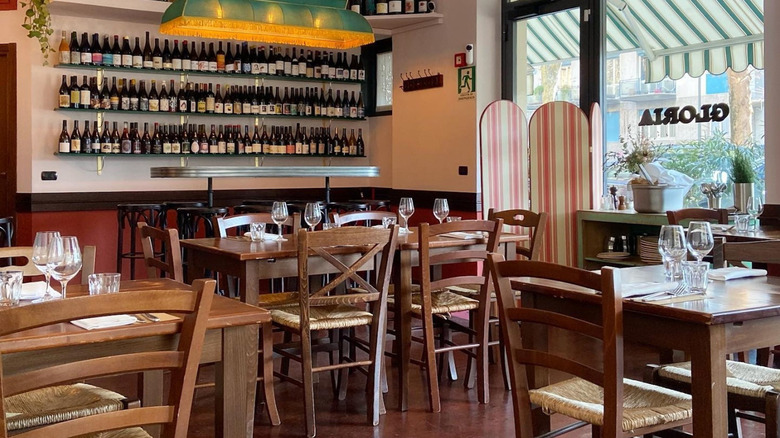 Restaurant tables and wine bottles on the wall at Trattoria della Gloria in Milan.