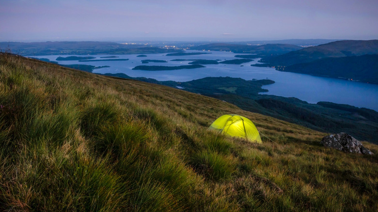 Near a Scottish loch, a tent glows in the fading light