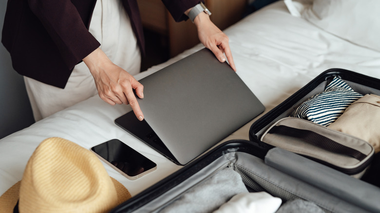 person folding laptop near suitcase