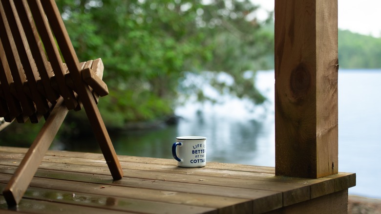 A cup of coffee rests on the wooden deck of a lakeside cabin