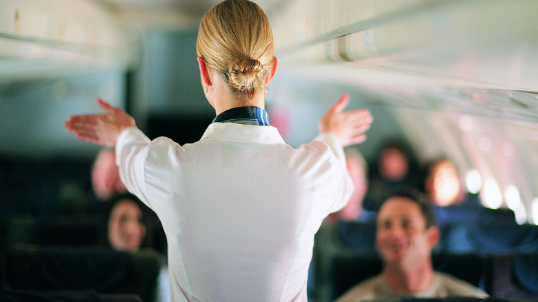 Fligth attendant gestures toward passengers in airplane cabin