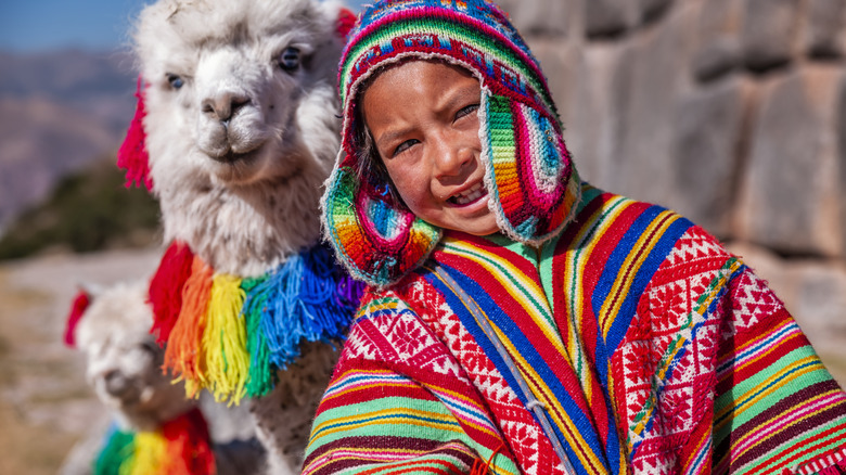 Child wearing colorful clothes posing next to llama