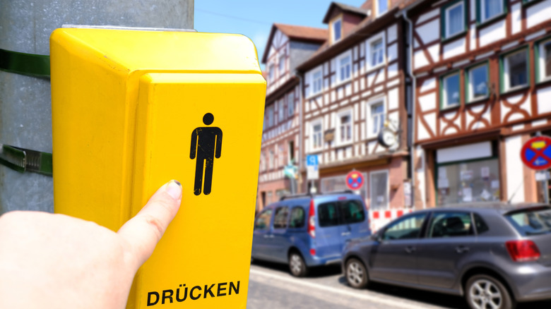 Person pushes yellow pedestrian light near half-timbered houses