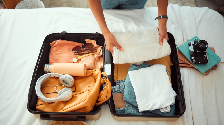person packing clothes in suitcase