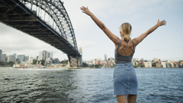 Woman standing with arms out in front of Sydney Harbour Bridge